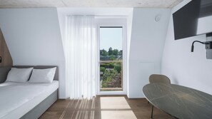 A modern hotel room with a bed, a dining table, a TV, and a balcony with a view of greenery. - Mooi Apartments Biel (Biel)