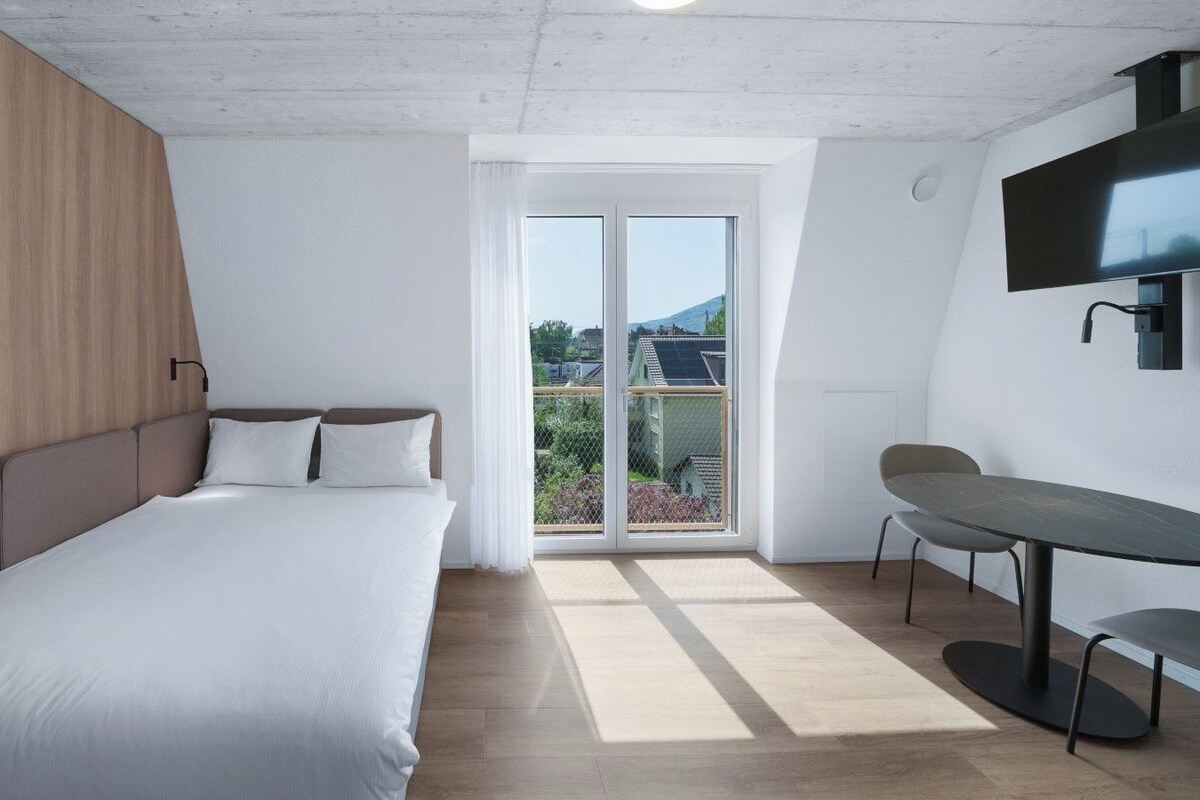 Un dormitorio moderno con una cama, un escritorio y vistas al exterior.