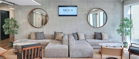 Ein modernes Wohnzimmer mit einem grauen Ecksofa, runden Spiegeln und einem Fernseher, der "MOOI Apartments" zeigt.