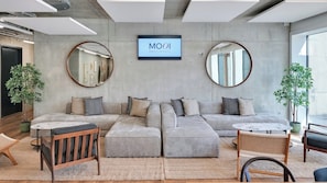 A modern living room with a grey sectional sofa, round mirrors, and a television displaying "MOOI Apartments". - Mooi Apartments Biel (Biel)