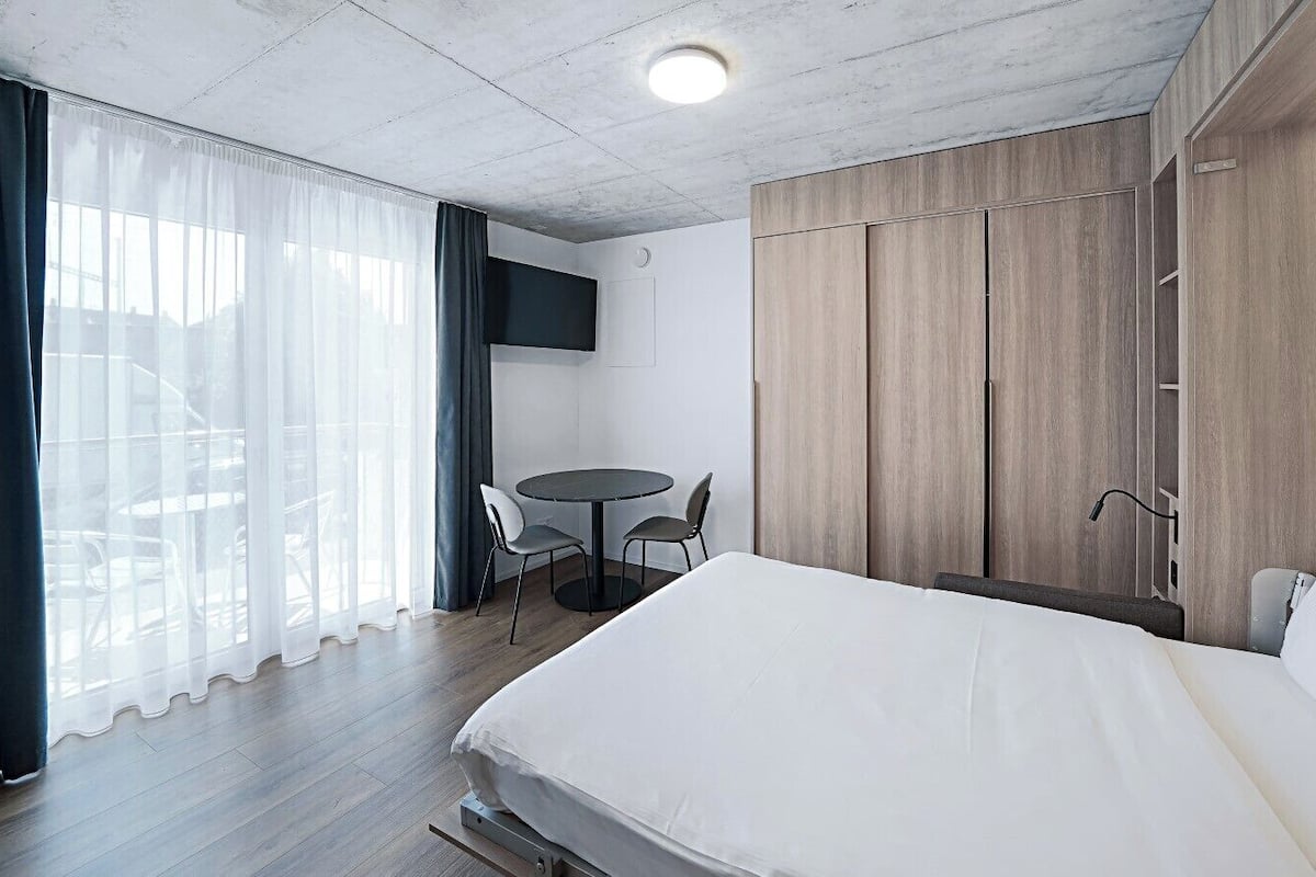 A hotel room with a large bed, a desk with two chairs, a TV mounted on the wall, and a wardrobe.