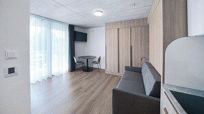 A modern room with a sofa, a round table with chairs, a TV mounted on the wall, and a window with curtains. - Mooi Apartments Biel (Biel)
