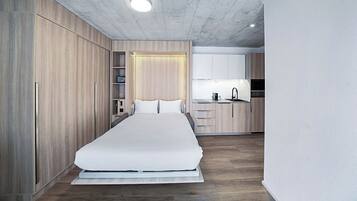 A modern bedroom with a large bed, wooden wardrobe, and a small kitchenette.