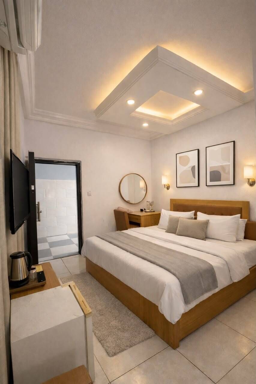 Una habitación de hotel moderna con una cama grande, mesitas de noche, un televisor e iluminación empotrada en el techo.