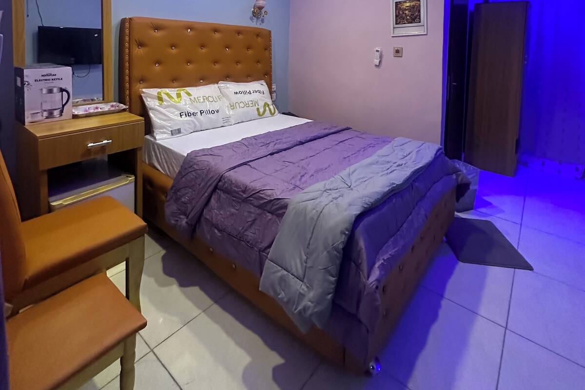 Ein Schlafzimmer mit einem Bett, einem Nachttisch, einem Stuhl, einem Schreibtisch und einem Spiegel.