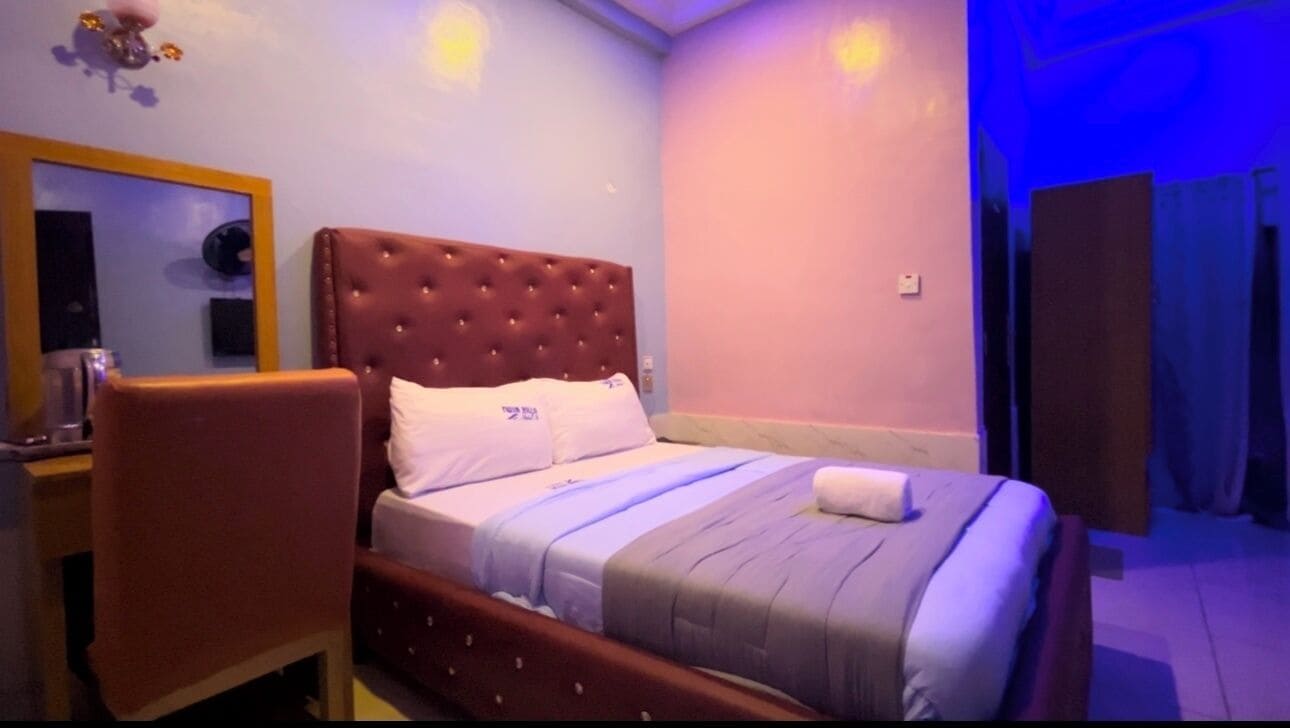 Camera d'albergo con un letto e una testiera trapuntata, un comodino, una sedia e uno specchio.