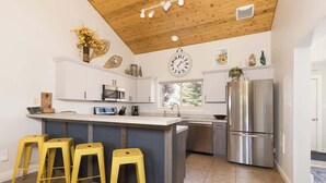 Une cuisine moderne avec des armoires blanches, un réfrigérateur en acier inoxydable et un plafond en bois.