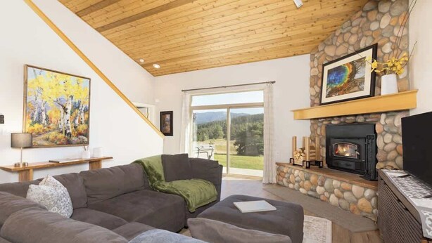 Un salon moderne avec une cheminée en pierre, un grand canapé et un tableau représentant une forêt.