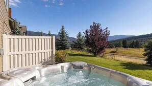 Un bain à remous dans un jardin, avec une clôture en bois, un arbre et une vue sur la montagne.