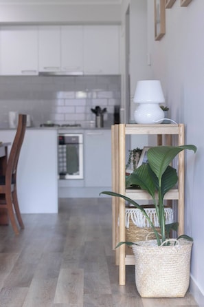 Kitchen features white cabinetry and a wooden floor, with a lamp and a woven basket with plants.