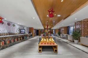 Un hall d’hôtel moderne doté d’un comptoir d’accueil central, d’un espace salon et d’un mur décoratif agrémenté d’éléments culturels.