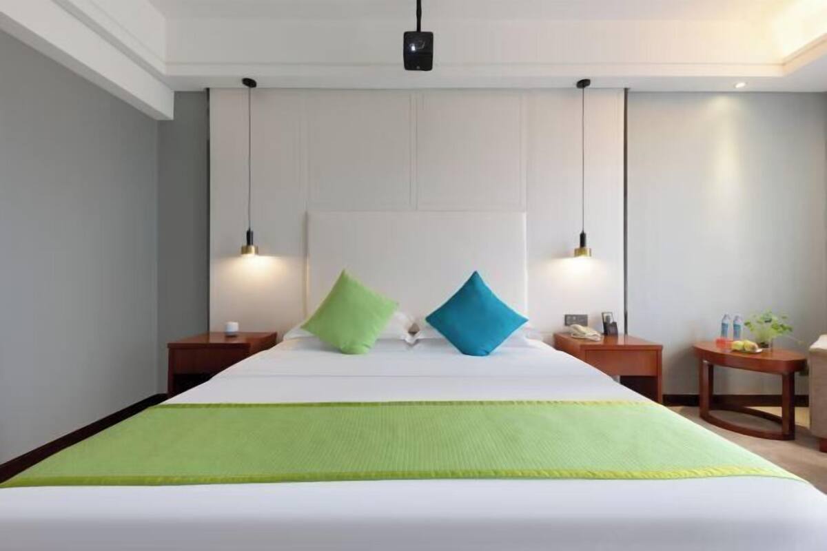 Habitación de hotel con una cama grande, dos mesitas de noche, un escritorio y una lámpara colgante.