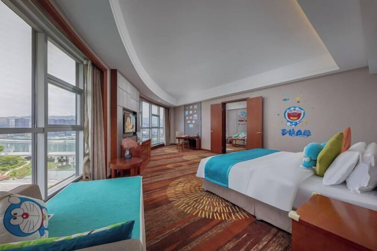 Una habitación de hotel con un ventanal grande, una cama, un escritorio y una silla.