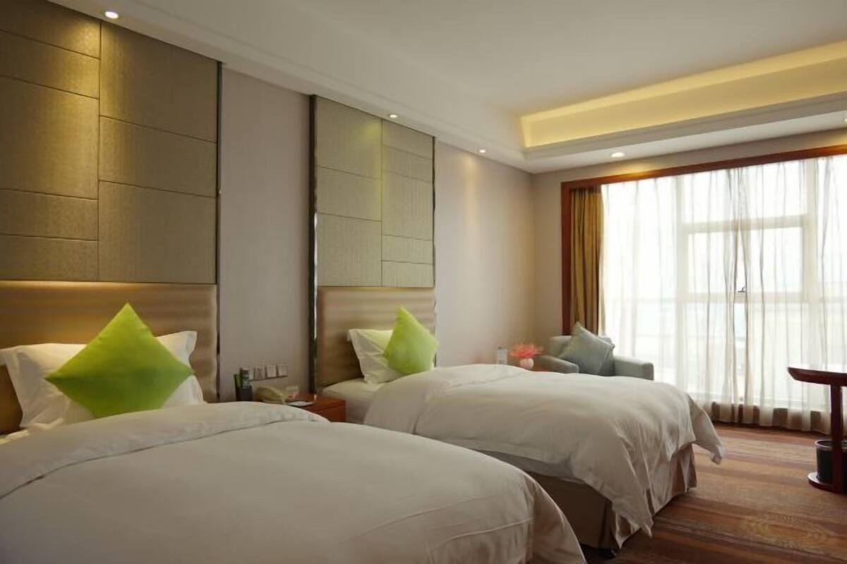 Habitación de hotel con dos camas, un sofá, una mesa y un ventanal grande con cortinas.