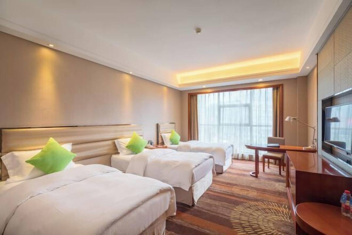 Habitación de hotel con dos camas, un escritorio, un televisor y un ventanal grande.