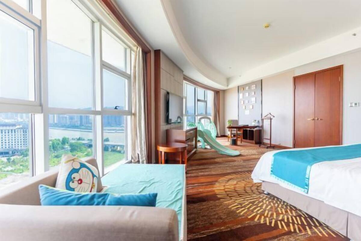 Una habitación de hotel con un ventanal grande, una cama, un sofá, un escritorio y una silla.
