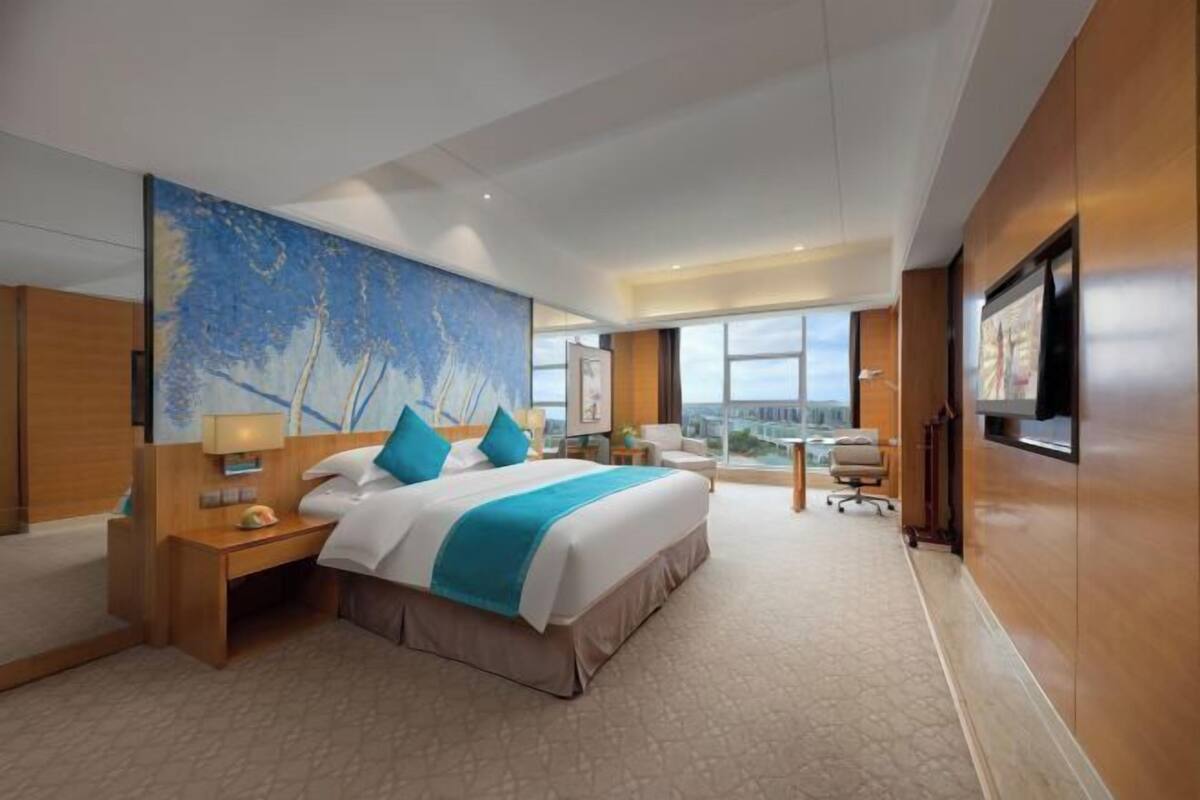 Habitación de hotel con una cama grande, un escritorio, una silla y un amplio ventanal con vistas a la ciudad.