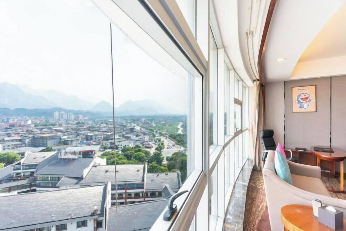 Habitación de hotel con un ventanal grande, un sofá, una mesita y una obra de arte colgada.