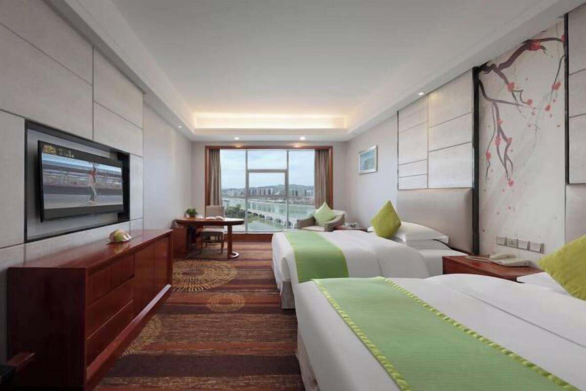 Habitación de hotel con dos camas, televisión, escritorio y vista a la ciudad.