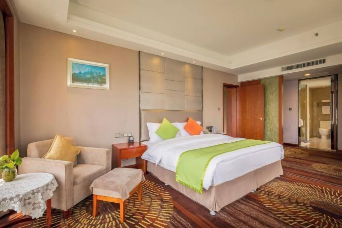Una habitación de hotel con cama, una silla, una mesita y un cuadro en la pared.