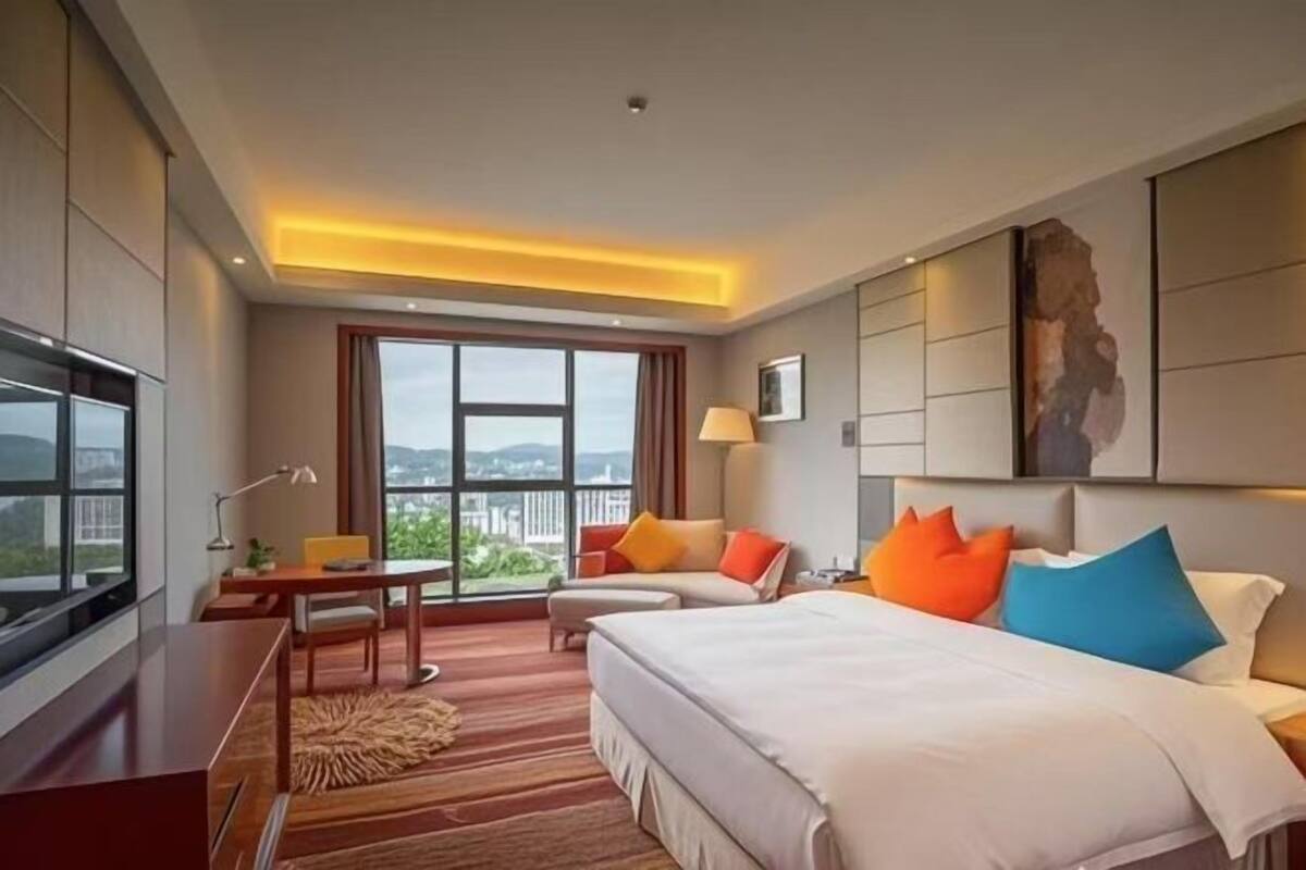 Habitación de hotel con una cama grande, un escritorio, una silla y vistas al exterior.