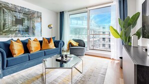 Una sala de estar moderna con un sofá azul, una mesa de centro de vidrio y un ventanal con vistas a la ciudad.