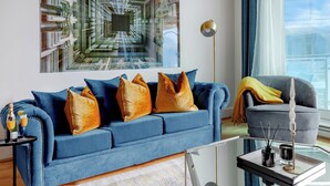 Una sala de estar moderna con un sofá azul, una mesa de centro de vidrio y un cuadro abstracto grande en la pared.