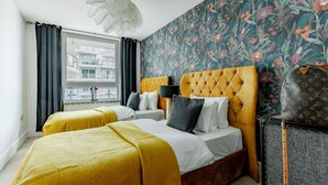 Habitación de hotel con dos camas, un ventanal grande, un papel tapiz floral y una maleta Louis Vuitton.