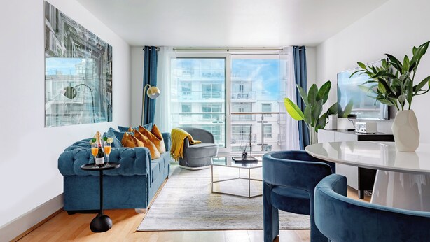 Una sala moderna con un sofá azul, una mesa de centro y una zona de comedor con una mesa blanca y sillas azules.