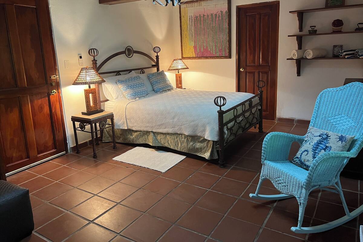 Une chambre à coucher avec un lit, deux lampes de chevet, un fauteuil à bascule et un plancher carrelé.