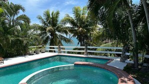 A swimming pool with a brick edge, surrounded by palm trees and a white fence. - B&B Casa Naturaleza Playa Corona (Las Uvas)