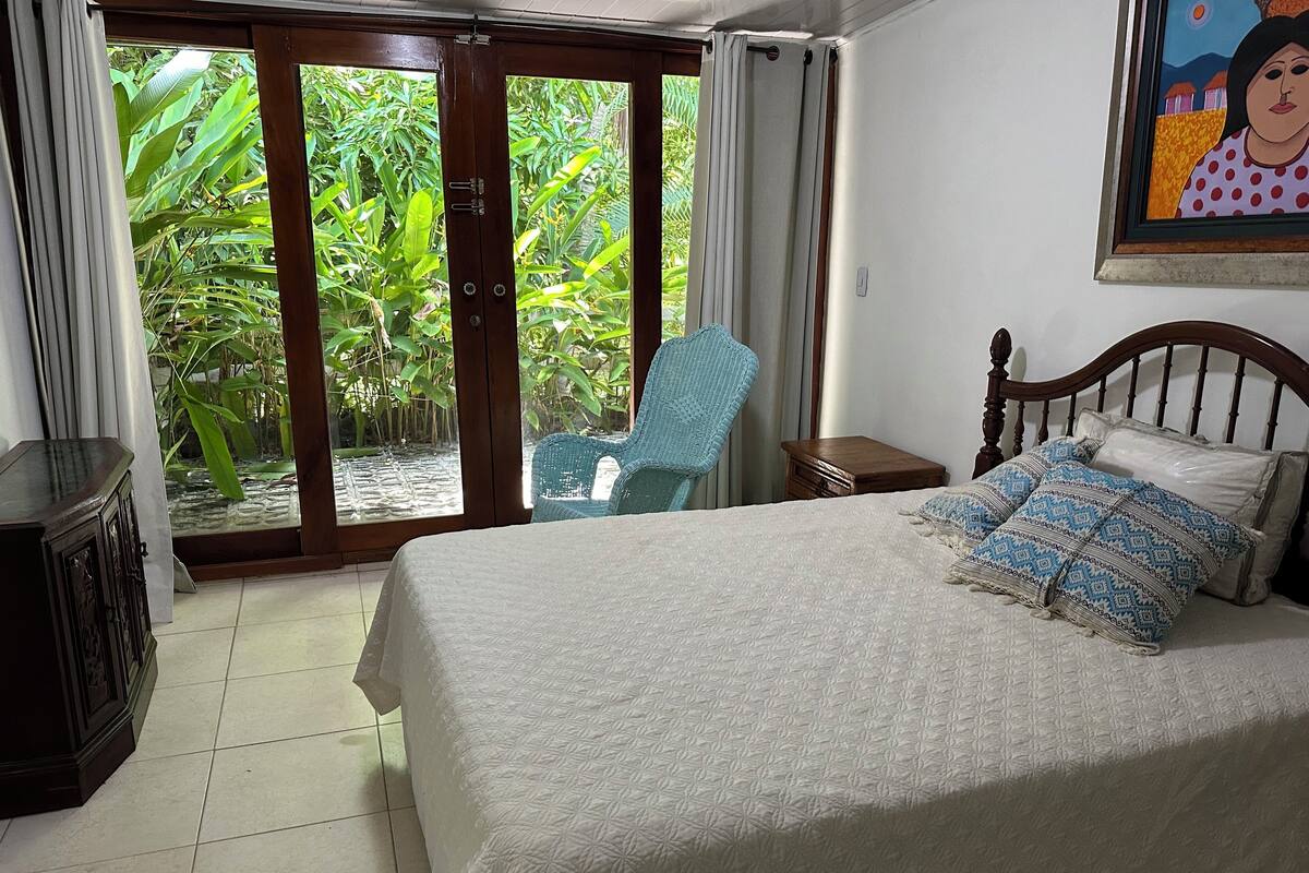 Une chambre à coucher comprenant un lit, une chaise, une table de chevet et une vue sur la verdure grâce à une porte coulissante.
