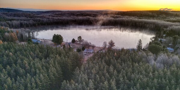 A lake surrounded by dense forest with houses near the water's edge. - Charming vacation home by the water—pets welcome! (Cayamant)