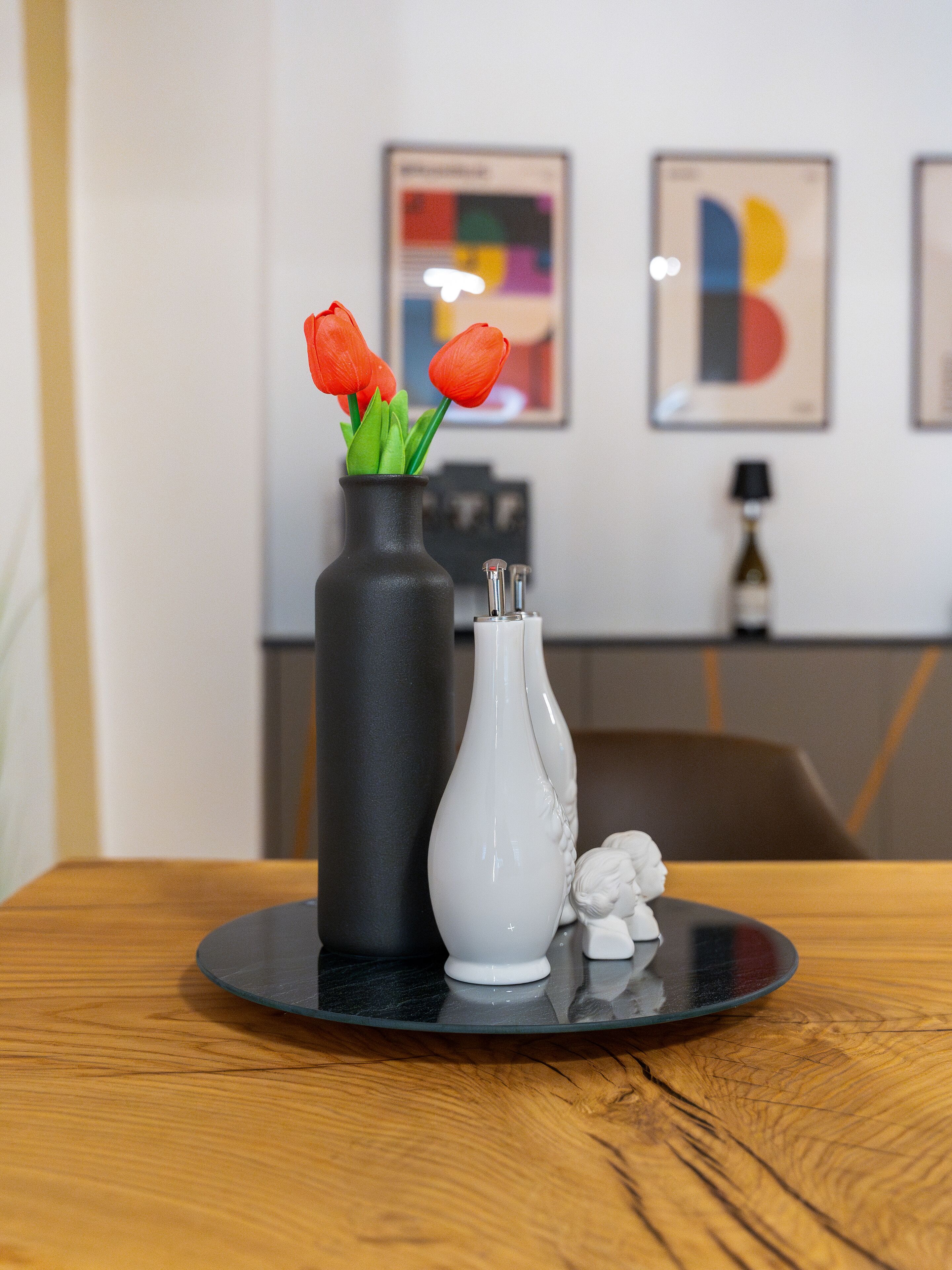 A table with a black vase containing red flowers and a white vase with a decorative figure.