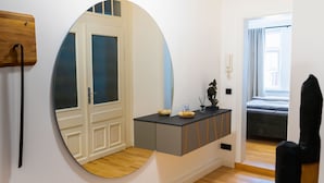 Een moderne kamer met een houten vloer, een ronde spiegel, een grijze console met decoratieve objecten, en een bed op de achtergrond.