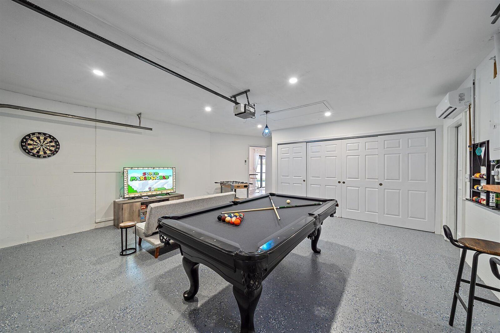 A pool table with billiard balls, a dartboard, and a television displaying a game.
