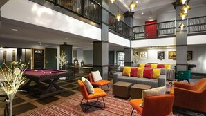 Eine großzügige Lobby mit Poolbillard, bequemen Sitzgelegenheiten und einer hohen Decke mit hängenden Lampen.