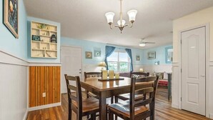 Un coin repas avec une table et des chaises en bois, un lustre et une cuisine en arrière-plan.