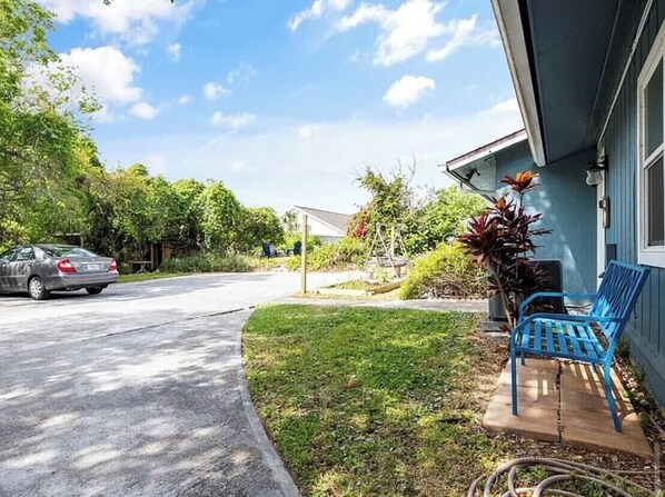 A residential driveway with a parked car, a lawn, a blue bench, and a house with a blue exterior.