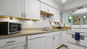 Une cuisine avec des armoires blanches, un four à micro-ondes, un évier et une cuisinière.
