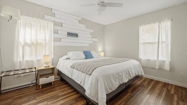 Une chambre à coucher comprenant un lit, une table de chevet, une étagère fixée au mur et un ventilateur de plafond.