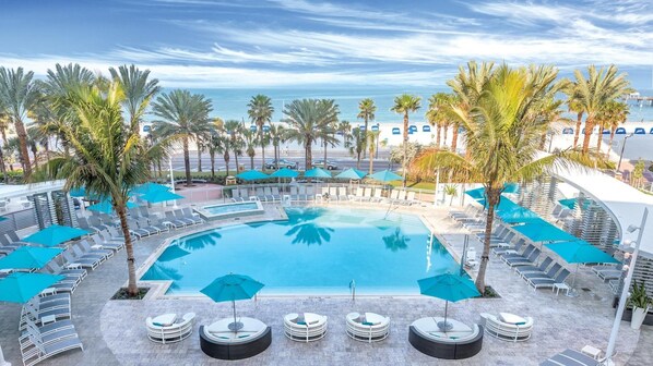 A pool area with lounge chairs and umbrellas, surrounded by palm trees and a view of the ocean. - Soak Up the Sunshine at Wyndham Clearwater Beach-1 Bedroom Deluxe (Clearwater)