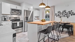 Una cocina moderna con armarios blancos, electrodomésticos de acero inoxidable, una isla de madera y taburetes negros.