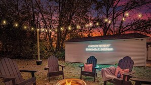 Un espacio exterior con asientos tipo Adirondack, un brasero y un cartel que muestra