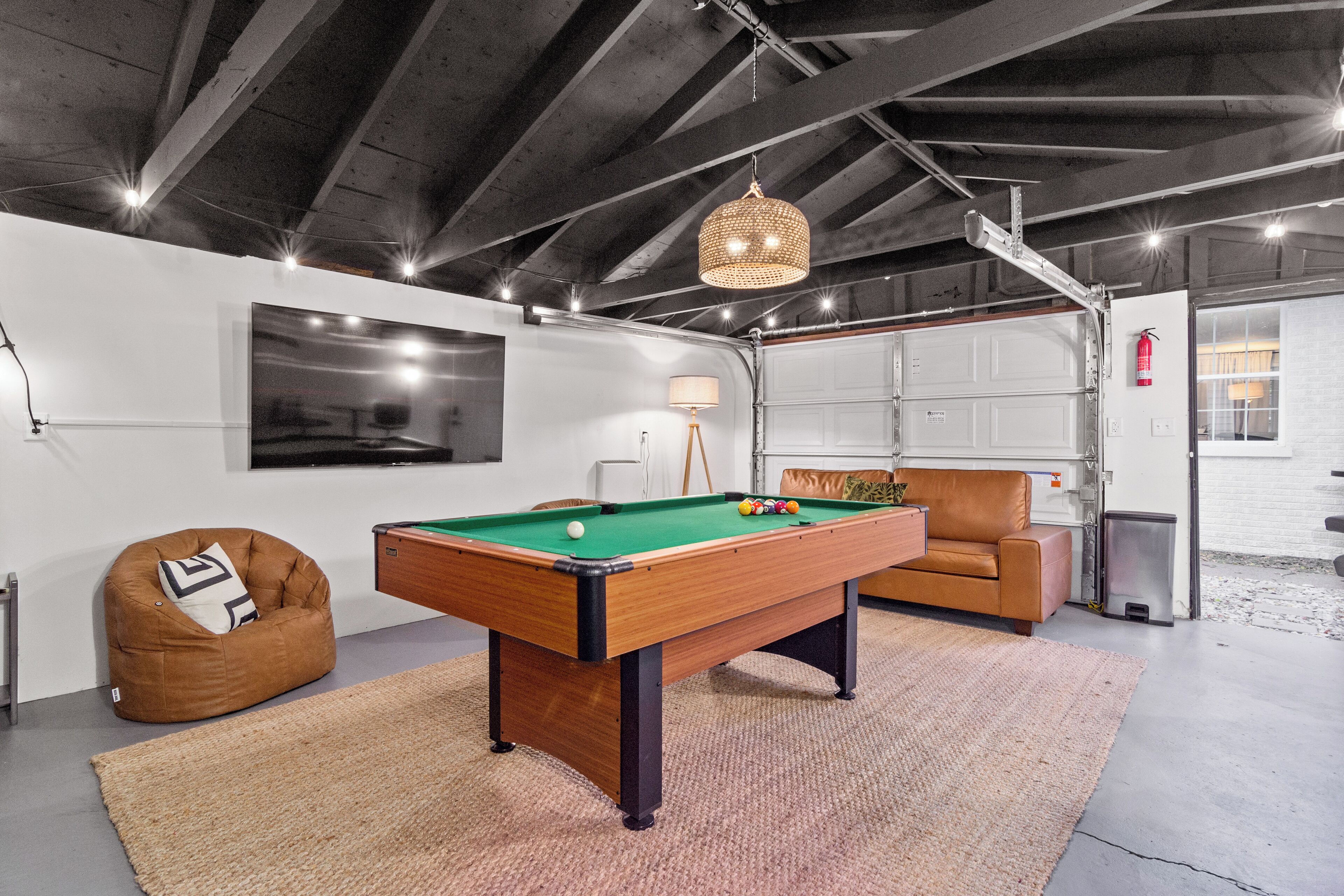 Une table de billard dans une pièce dotée d’un plafond haut, d’un luminaire suspendu, d’un canapé et d’un extincteur.