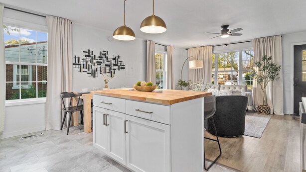 Una cocina moderna con armarios blancos, encimera de madera e iluminación colgante.