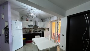 A compact kitchen with white cabinets, a white dining table, and a black door. - Apartment in front of the sea (Siderno)
