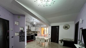 A modern kitchen with white cabinets, a dining area with a white table and chairs, and a red chair. - Apartment in front of the sea (Siderno)