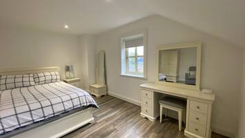 A bedroom with a bed, dresser, vanity, and a window.