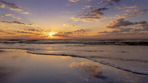 Ein Strand bei Sonnenuntergang mit Wellen und Wolken.